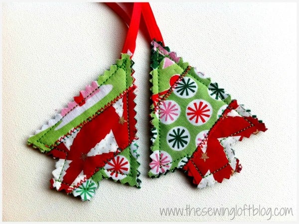 Two patchwork Christmas tree ornaments, inspired by quilt patterns and made from colorful fabric scraps stitched with zigzag seams, hang from red ribbons on a white background.
