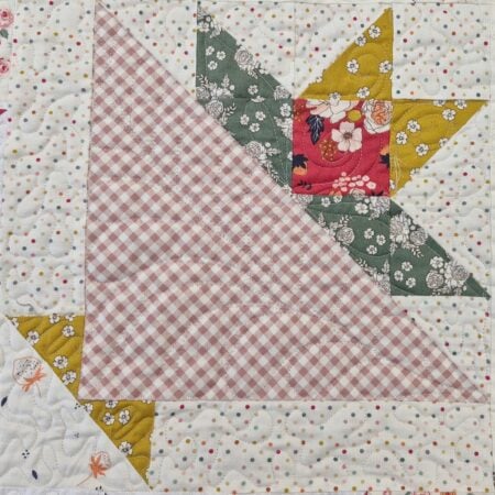 A quilt block for the June 2026 BOM, featuring a pink and white gingham triangle, floral green and yellow triangles, and a white background with colorful dots and small orange flowers in a geometric basket pattern.