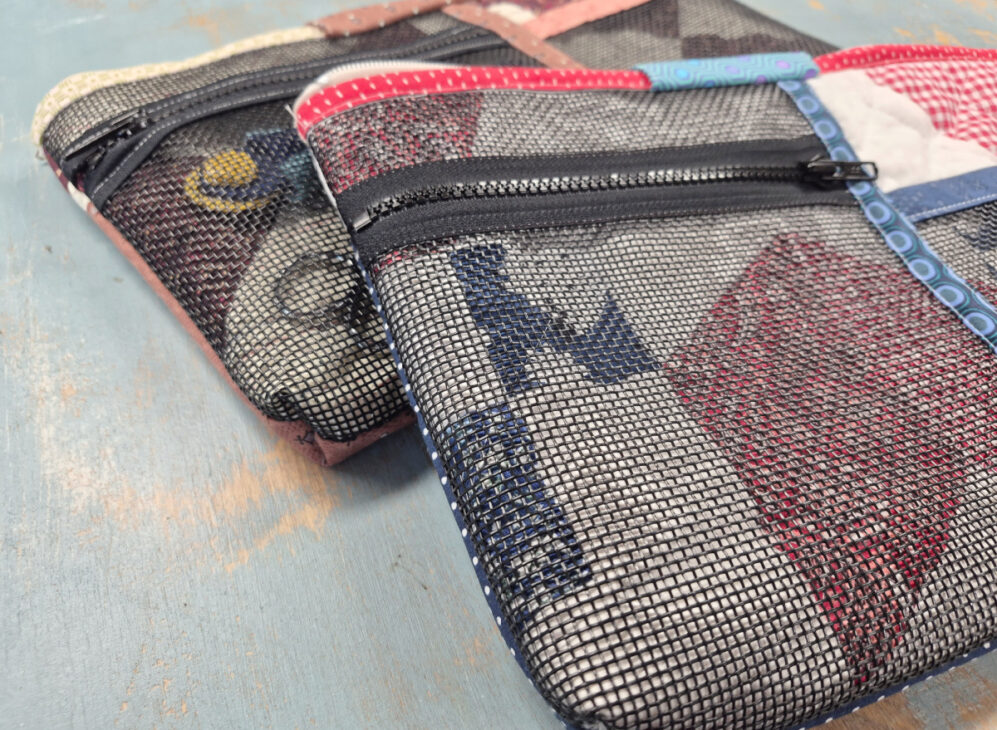 Two zippered pouches made of mesh fabric with colorful patchwork designs rest on a worn blue surface. Each Notion bag pattern reveals vibrant patterns and colors inside, perfect for organizing your creative essentials.