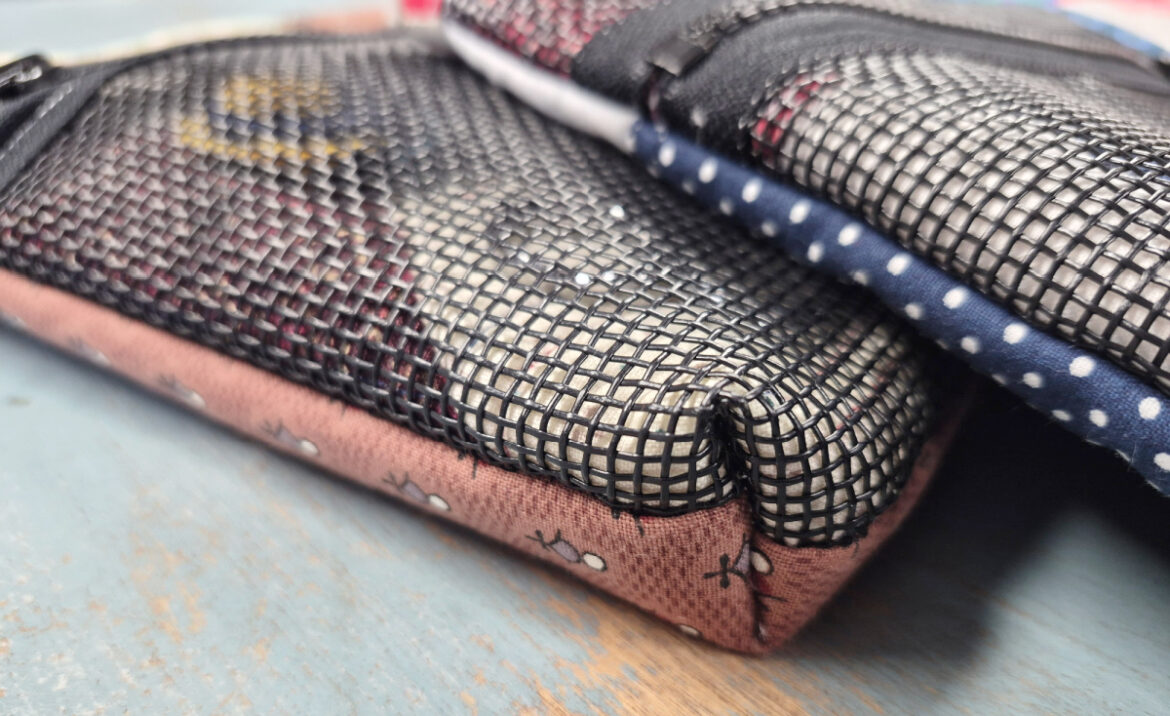 Close-up of two zippered pouches with mesh covers—perfect as a notion bag for your next sewing day. One features a pink base with small patterns, the other navy blue with white polka dots. Both rest on a light blue surface.
