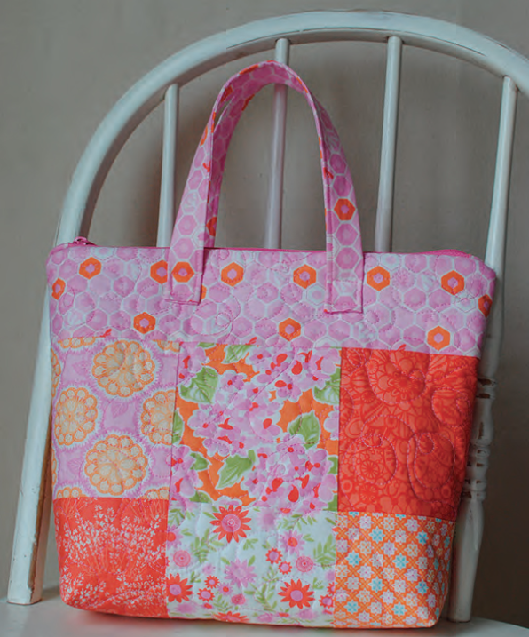 Easy and Cute Lunch Bag Sewing Patterns You'll Want to Make and Use 14 A colorful patchwork tote bag with pink, orange, and floral fabric squares, displayed on a white wooden chair against a neutral background—perfect inspiration for cute lunch bag or easy lunch bag sewing patterns.