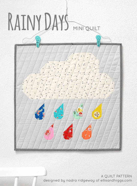 Mini Quilt Patterns You'll Want to Make This Weekend 16 A quilted wall hanging features a polka dot cloud with colorful patchwork raindrops on a gray striped border, displayed on a wall with a blue cloud hanger. Text reads "Rainy Days Mini Quilt" and mini quilt patterns and details.