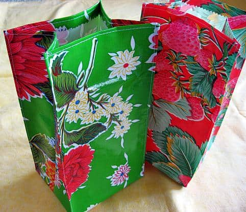 Easy and Cute Lunch Bag Sewing Patterns You'll Want to Make and Use 12 Two colorful tote bags, one green with white and red flowers, and one red with strawberries and leaves, are standing upright on a yellow surface—perfect inspiration for anyone looking for easy sewing patterns or dreaming of making their own cute lunch bags.