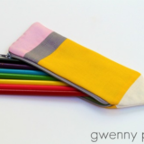 A pencil-shaped zippered pouch contains six colored markers (green, blue, black, yellow, red, and pink) on a white background. Perfect for those who love to make their own accessories, this Pencil pouch is a fun project idea inspired by sewing patterns. The words "gwenny penny" appear in the bottom right corner.