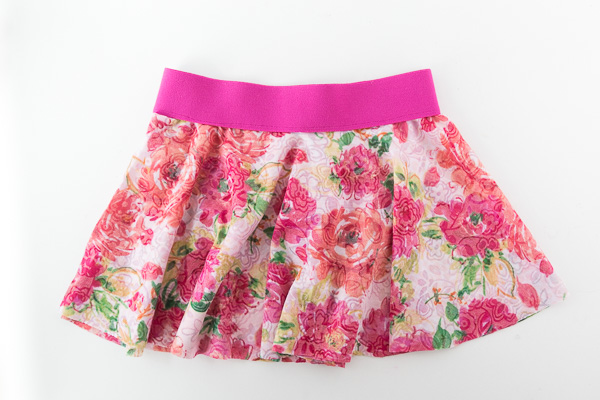 15 Easy Elastic Waist Skirt Patterns You Can Sew Today (All Free) 6 A floral patterned skirt with shades of pink, red, and green, featuring a wide, bright pink waistband and crafted using easy skirt sewing techniques, displayed on a white background.