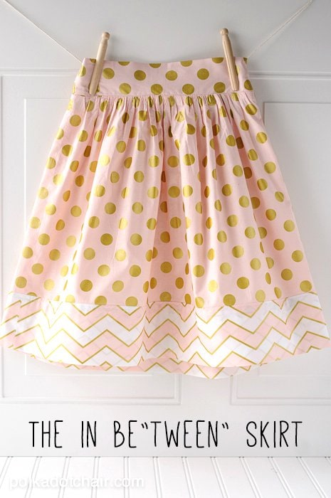15 Easy Elastic Waist Skirt Patterns You Can Sew Today (All Free) 10 Light pink skirt with gold polka dots and a chevron pattern at the hem, hanging by clothespins on a line. Featuring an elastic waist for comfort, this design is perfect for those searching for easy skirt sewing inspiration. Text at the bottom reads "THE IN BETWEEN SKIRT.