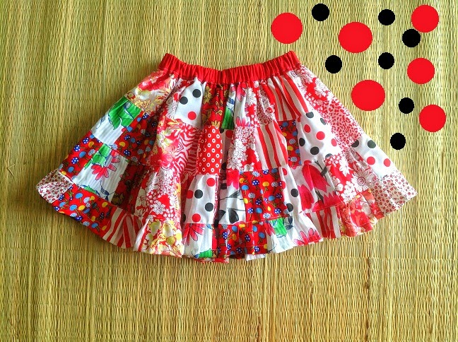 15 Easy Elastic Waist Skirt Patterns You Can Sew Today (All Free) 14 A colorful, patterned skirt with a red waistband, inspired by easy skirt patterns, lies on a woven mat. In the top right corner, there are six red circles and two black circles arranged in a grid pattern.