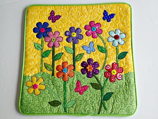 Refresh Your Home with These Summer Pillow Sewing Ideas (free patterns) 10 A colorful quilted mat featuring bright flowers, green stems, leaves, and butterflies on a yellow and green background with swirling patterns—perfect for a cheerful home refresh or as inspiration for summer pillow sewing.