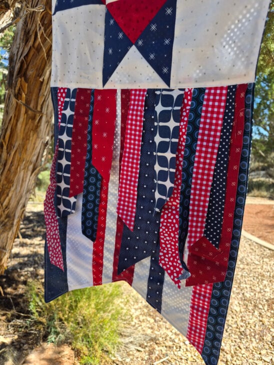 Seasonal Ribbon Banner – A Fun Way to Celebrate Every Season 4 A Seasonal Ribbon Banner hangs outside, featuring red, white, and blue patterns, including stars and stripes, against a tree and greenery background—a perfect way to Celebrate Every Season with festive style.