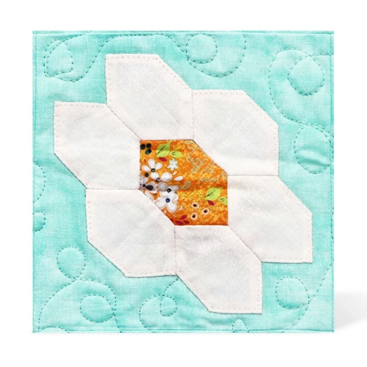 English Paper Piecing Honeycomb-1" Finished Sides Die AccuQuilt 3 A quilt square featuring a white flower with six petals and an orange patterned center, set against a light blue background with swirly quilted stitching—expertly crafted using the AccuQuilt system for precise cutting.