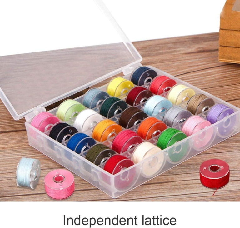 Bobbin Storage Ideas That Will Finally Keep Those Threads Under Control 4 A plastic box with rows of colorful sewing thread spools is open on a wooden surface, showcasing practical thread organization. Three spools—blue, pink, and red—are outside the box. The box contains 25 spools in various colors, offering inspiration for clever sewing room ideas.