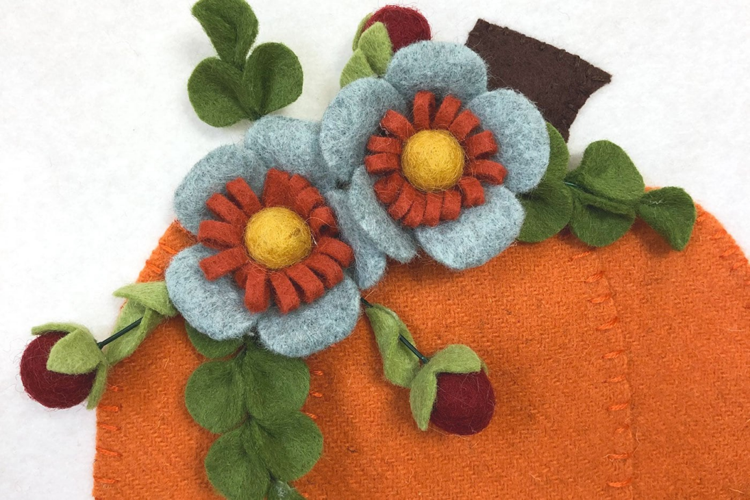 Fall Appliqué Patterns That Are Perfect for Your Fabric Scraps 12 Felt craft showing an orange pumpkin with blue and red felt flowers, yellow centers, green leaves, and small red berries, all on a white background—perfect as a charming fall applique.