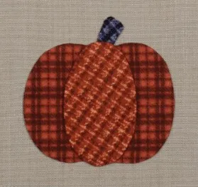 Fall Appliqué Patterns That Are Perfect for Your Fabric Scraps 8 A fabric fall applique of a pumpkin features a plaid orange pattern and a blue plaid stem, set against a beige background.