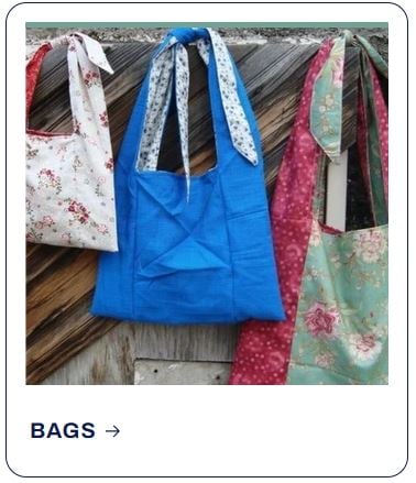 Three handmade fabric tote bags with decorative patterns hanging on a wooden wall.