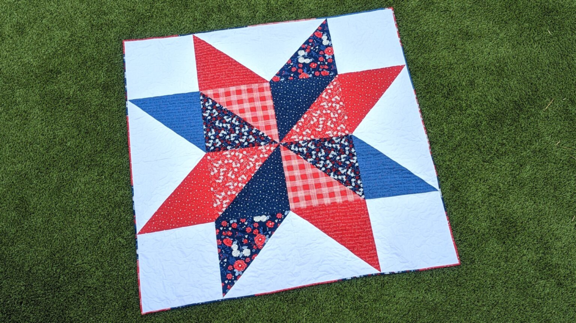 Veterans Day Sewing Projects to Honor Those Who Served 5 A square quilt featuring a red, white, and blue lone star pattern displayed on a grassy surface as a patriotic sewing project to honor veterans.