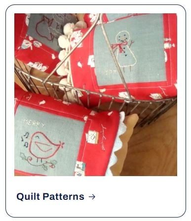 Red fabric sachets with embroidered snowman and bird designs displayed in a wire basket, inspired by festive shop patterns.